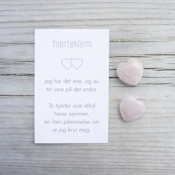 Et kort med teksten “hjertklem” og to rosa steinhjerter ved siden av, på lyst treverk.