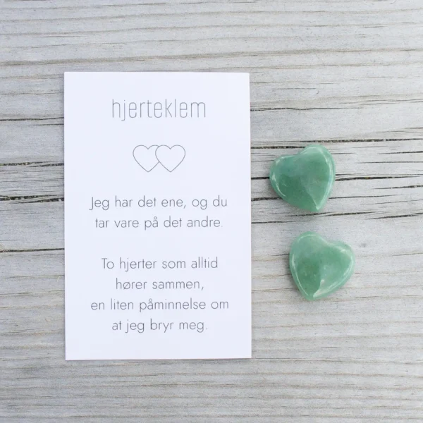 Et kort med teksten “hjertklem” og to grønne steinhjerter ved siden av, på lyst treverk.