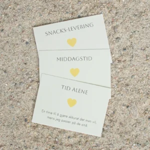 Tre gule hjertelapper med teksten “Snacks-levering”, “Middagstid” og “Tid alene”, liggende på sand. Hver lapp har et gult hjerte og enkel, sort tekst.