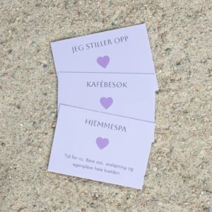 Tre lilla hjertelapper med teksten “Jeg stiller opp”, “Kafébesøk” og “Hjemmespa”, liggende på sand. Hver lapp har et lilla hjerte og enkel, sort tekst.
