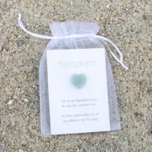 En hvit gavepose med kort og ett grønt krystallhjerte foran på kortet.