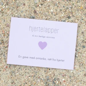 Kort med lilla hjerte og teksten «hjertelapper – til min herlige venninne», fotografert på sand.