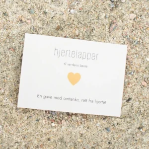 Kort med oransje hjerte og teksten «hjertelapper – til verdens beste», fotografert på sand.