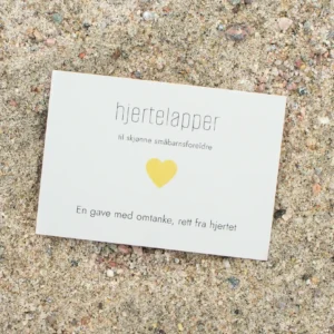 Kort med teksten «hjertelapper – til skjønne småbarnsforeldre» og et gult hjerte, fotografert på sand.