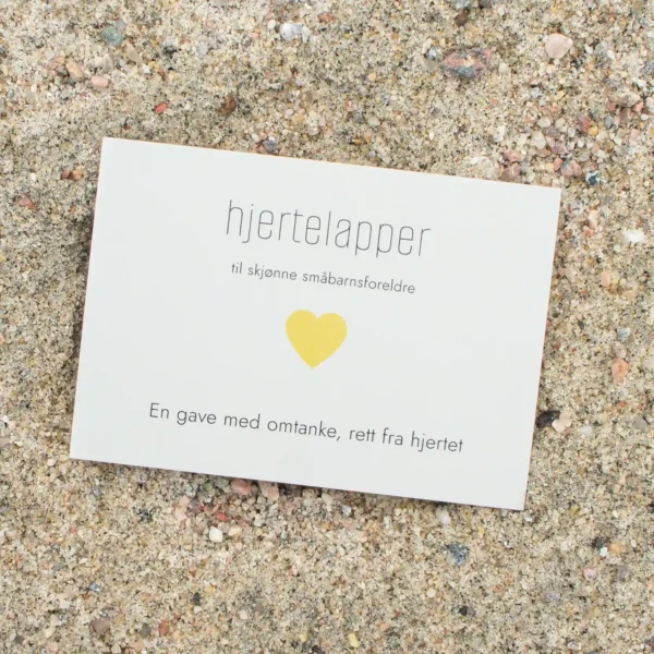 Kort med teksten «hjertelapper – til skjønne småbarnsforeldre» og et gult hjerte, fotografert på sand.