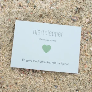 Kort med grønt hjerte og teksten «hjertelapper – til min kjære nabo», fotografert på sand.
