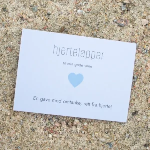 Kort med blått hjerte og teksten «hjertelapper – til min gode venn», fotografert på sand.