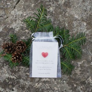 Juleklem med rødt hjerte i gjennomsiktig gavepose, pyntet med grankvister og kongler.