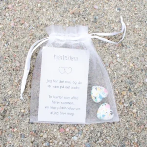 En hvit gavepose med kort og to små fargerike hjerter i, plassert på sand.