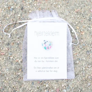 En hvit gavepose med kort og ett fargerikt hjerte foran på kortet.