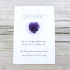 Kort med teksten “hjerteklem” og en dyp lilla hjertestein limt på, lagt på lys trebakgrunn. Kortet sier: “Her er en hjerteklem som du kan ha i lommen din. En liten påminnelse om at jeg alltid er her for deg.”